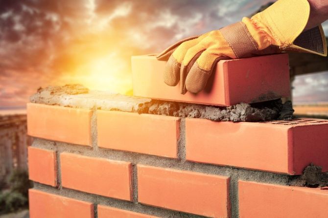 Construction worker laying a brick on a wall at sunset with bright glowing light