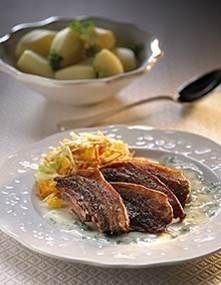 Grillet kød med revne grøntsager på tallerkenen, ved siden af en skål kogte kartofler på et bord