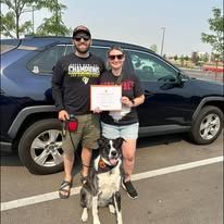 A man and women standing with their black and white dog holding a training certificate.