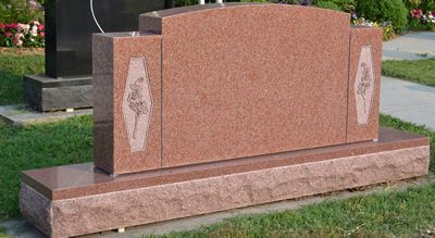 A red granite gravestone is sitting in the grass in a cemetery.