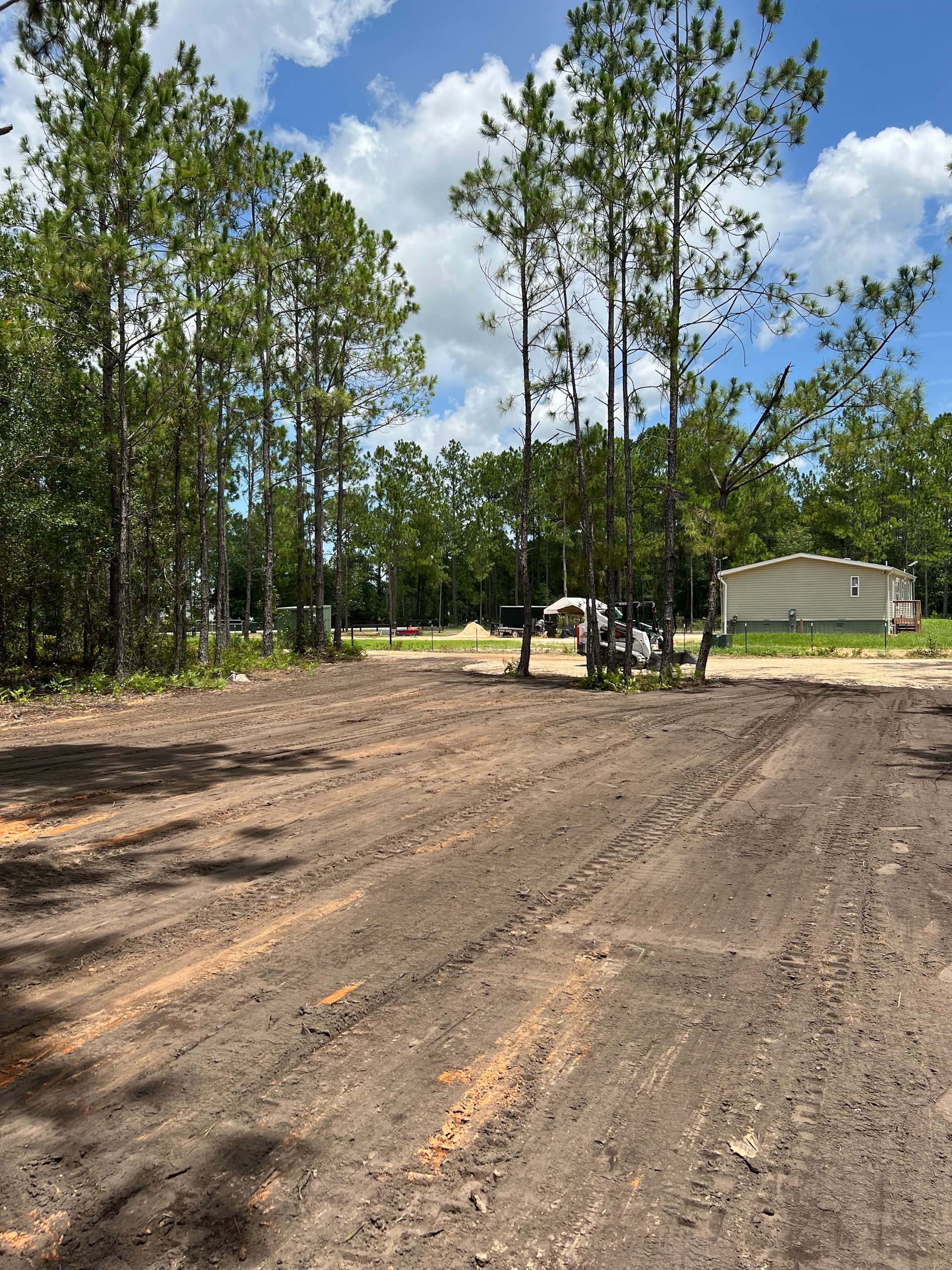 A dirt road with trees and a house in the background. - Midland Contractors - Clermont, FL