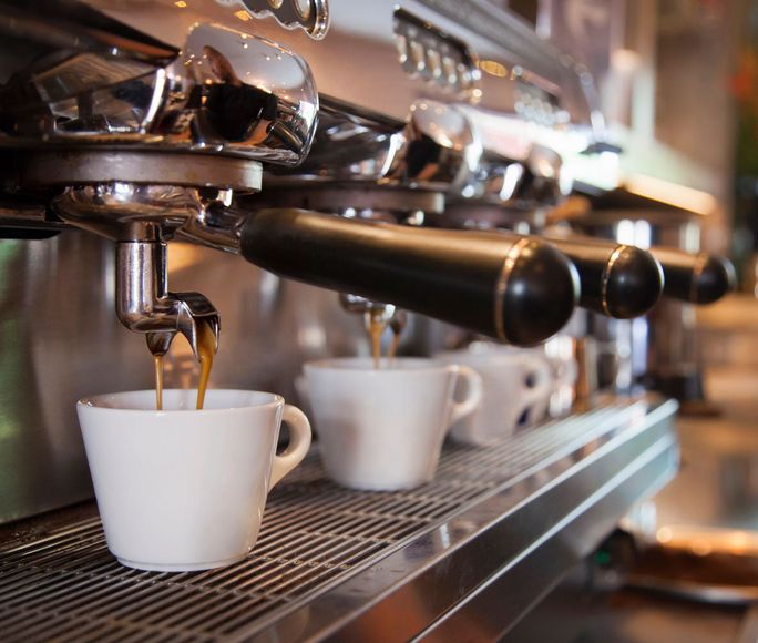 Macchina per caffè espresso che versa il caffè in tazze bianche su uno scaffale di metallo.