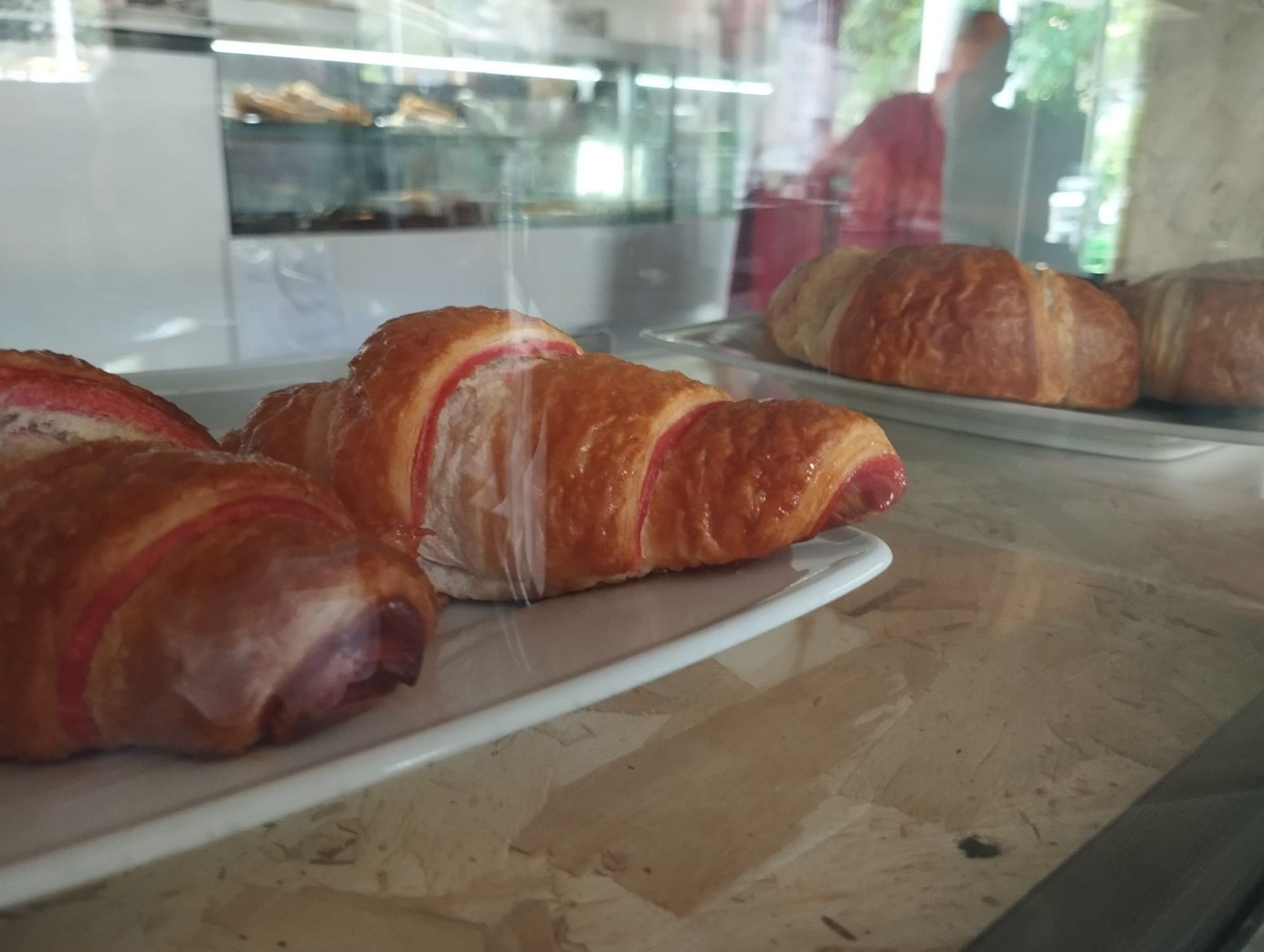 Cornetti su piatti bianchi dietro una vetrina in una panetteria. Alcuni croissant hanno il ripieno rosa.
