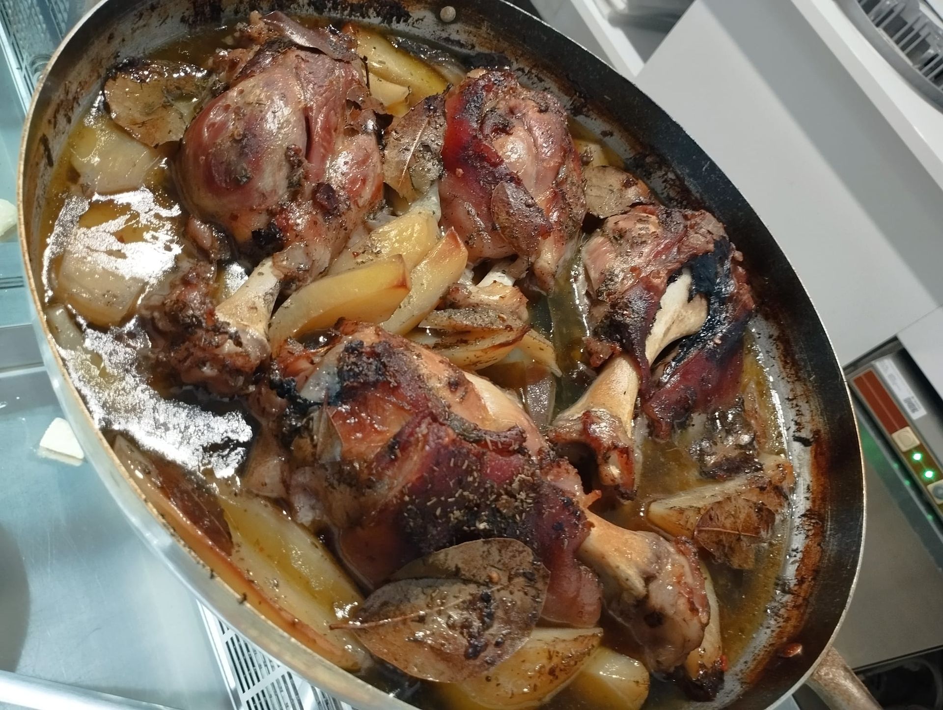 Stinco di agnello arrosto con patate in una padella di metallo, luccicante di sugo.