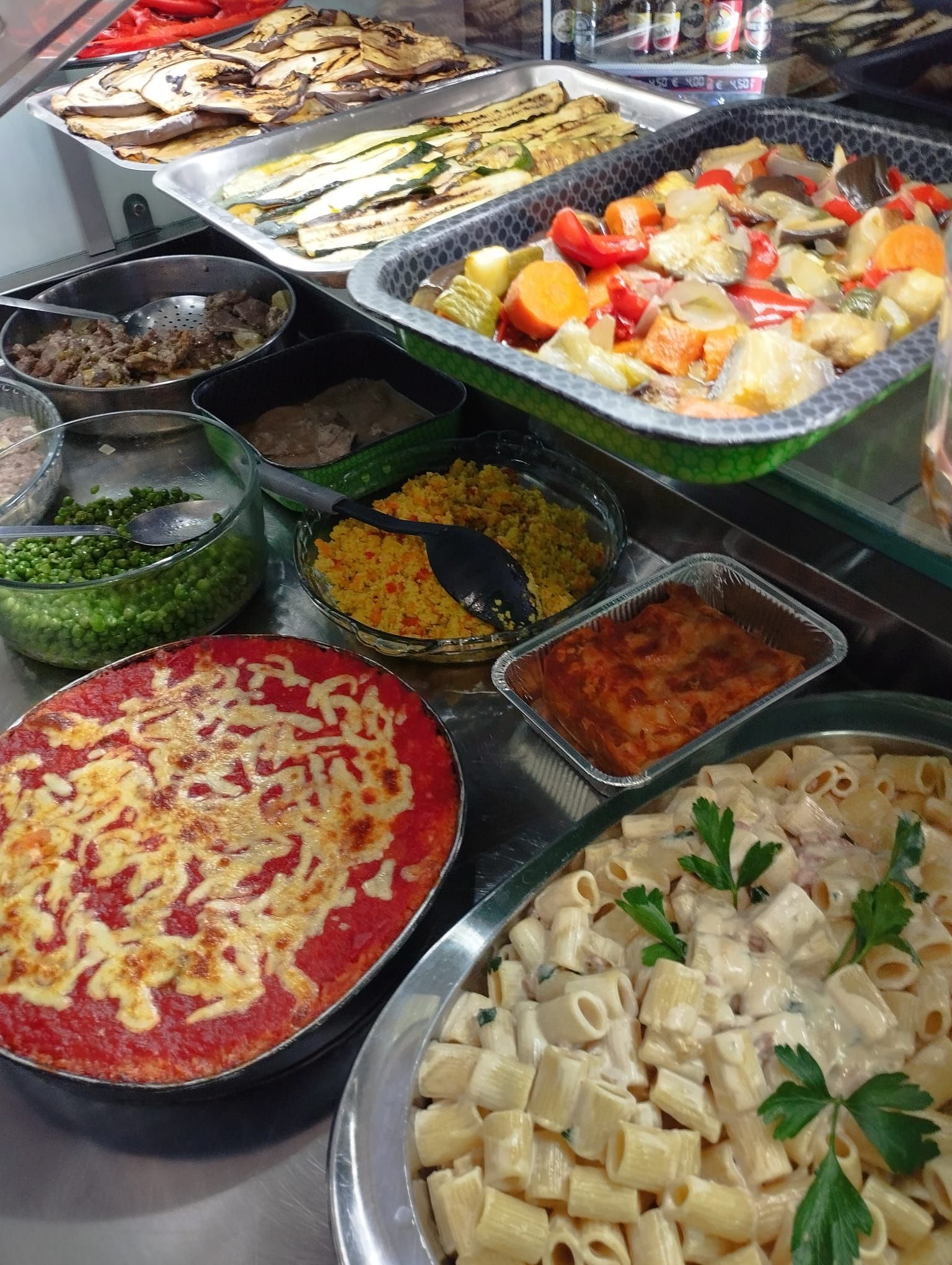 Esposizione di vari cibi preparati a buffet. Include verdure, pasta e stufati.