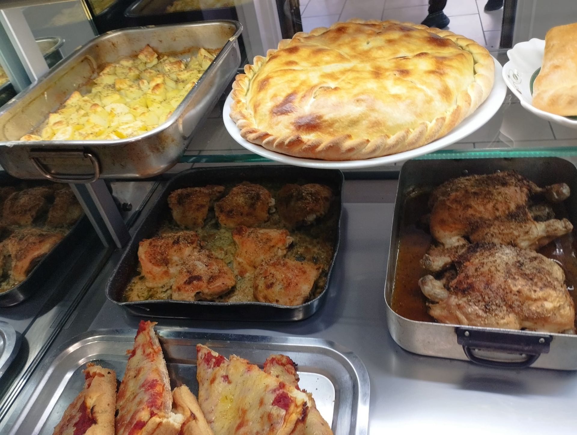 Esposizione di vari piatti cucinati, tra cui una grande torta, pollo al forno e casseruole, in un ambiente di ristorazione.