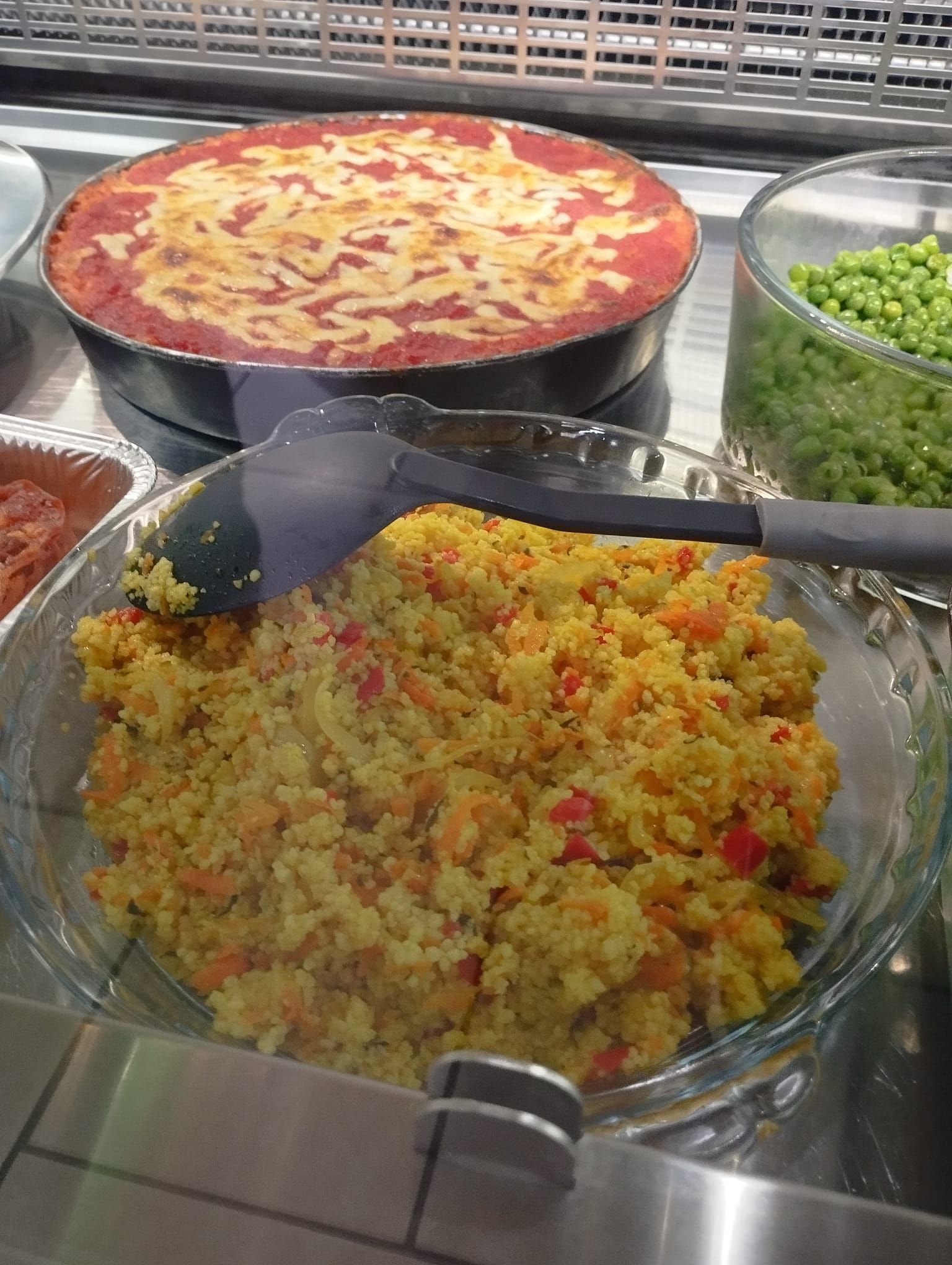 Vetrina con una ciotola di vetro di couscous giallo, una pentola di casseruola ricoperta di salsa rossa e una ciotola di piselli verdi.