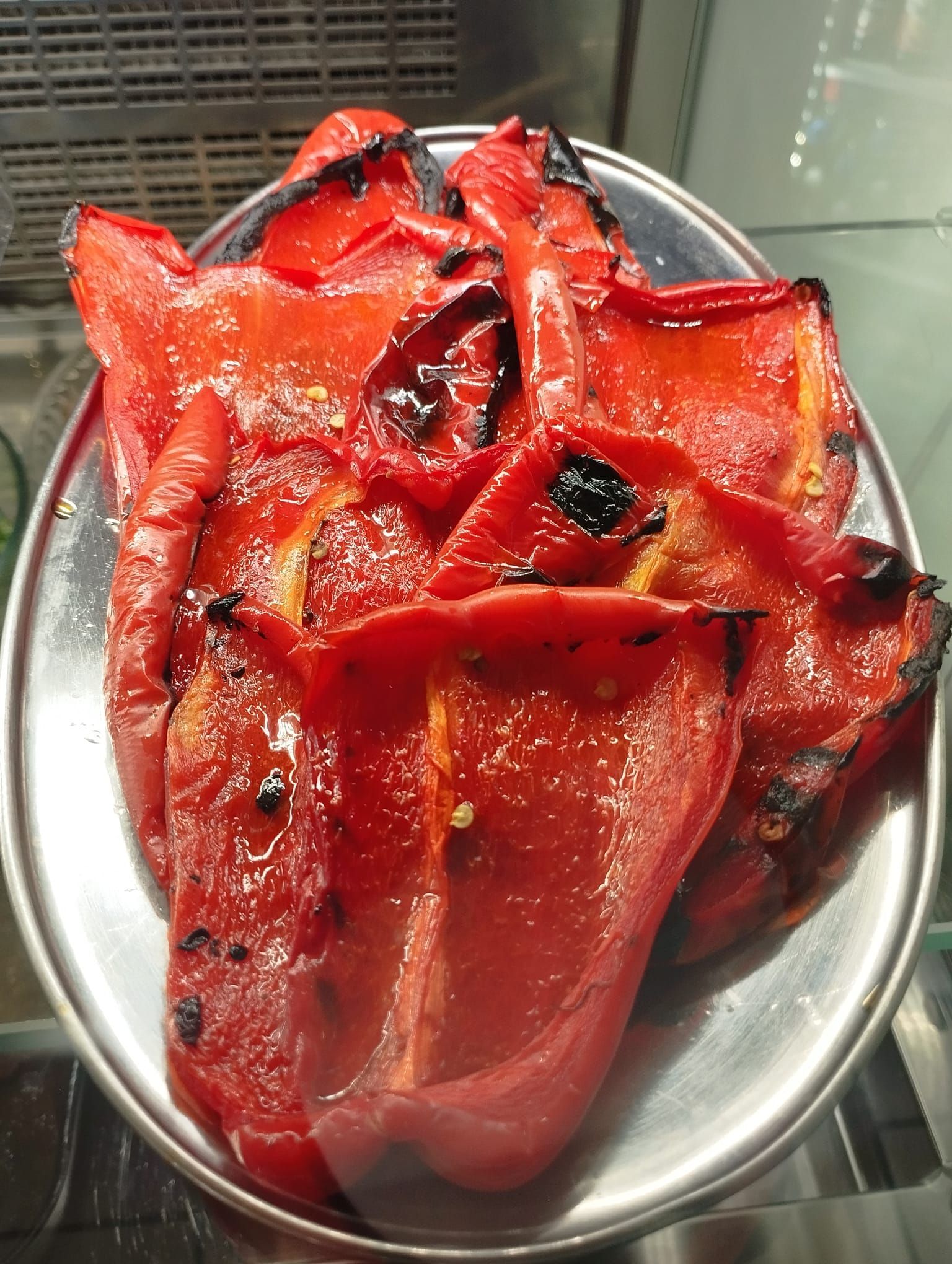 Peperoni rossi arrostiti su un piatto d'argento, con macchie bruciacchiate e superficie lucida.