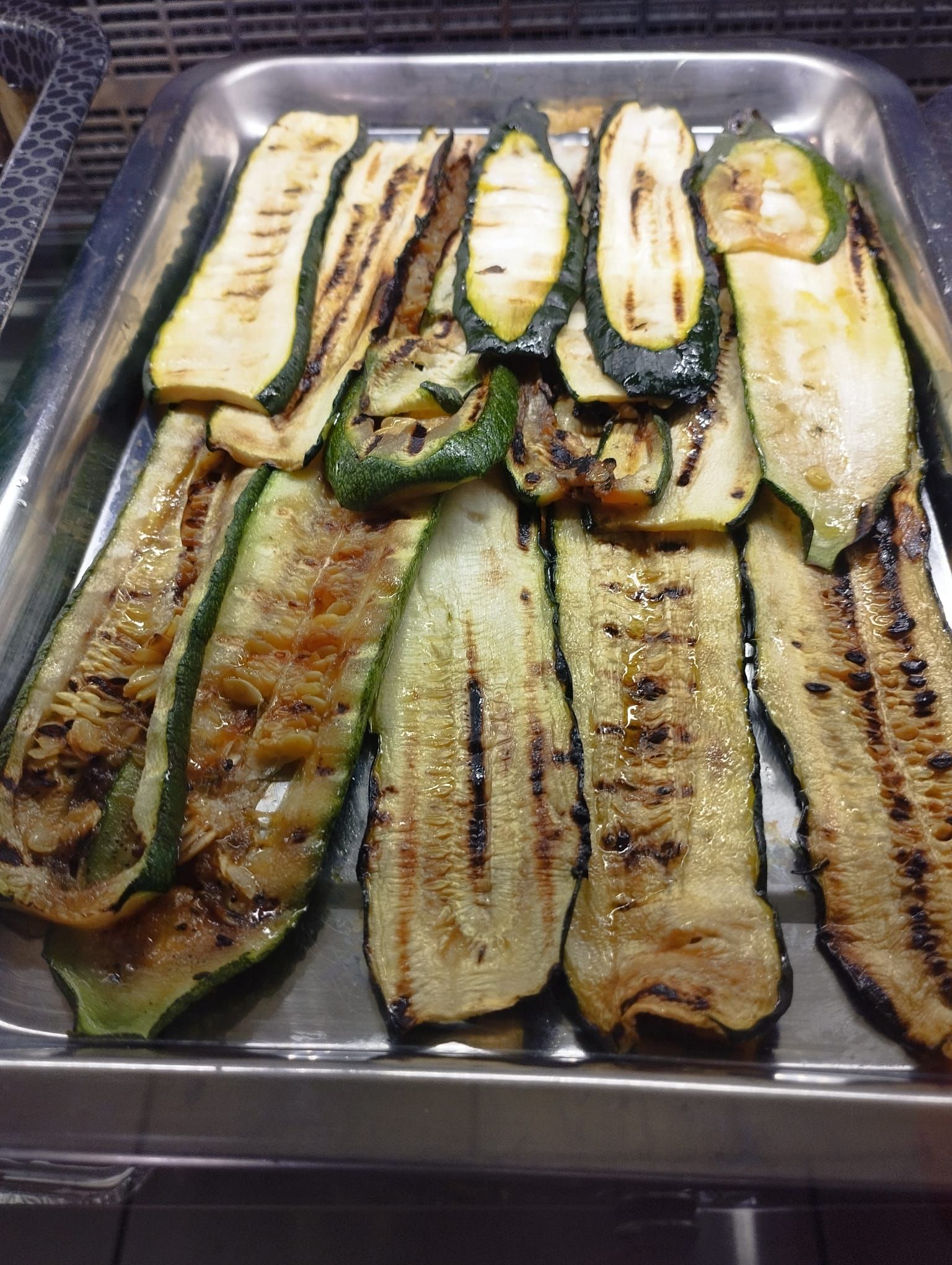 Fette di zucchine grigliate disposte su una teglia di metallo. Le fette sono verdi e dorate, con i segni della griglia.