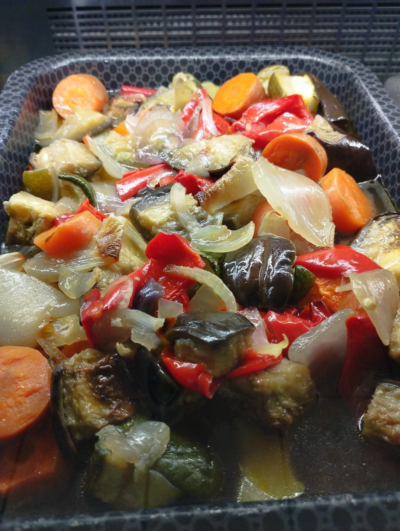Un vassoio di verdure miste arrostite, tra cui peperoni rossi, melanzane, carote e cipolle.