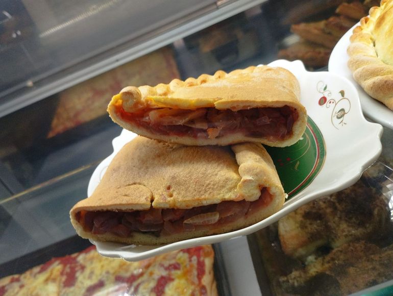 Due metà di un'empanada dorata su un piatto bianco decorativo, che rivelano un ripieno di salsa rossa e carne.