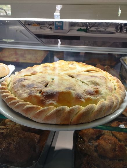 Una torta salata dorata con una crosta intrecciata è adagiata su un piatto bianco all'interno di una vetrina di vetro.