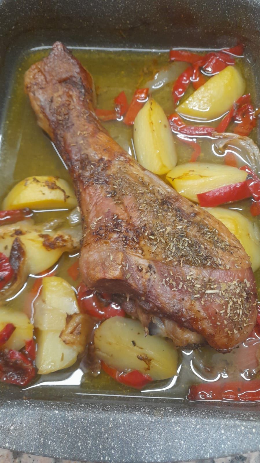 Coscia di tacchino arrosto con patate e peperoni rossi in una teglia da forno, ricoperta di succhi di cottura.
