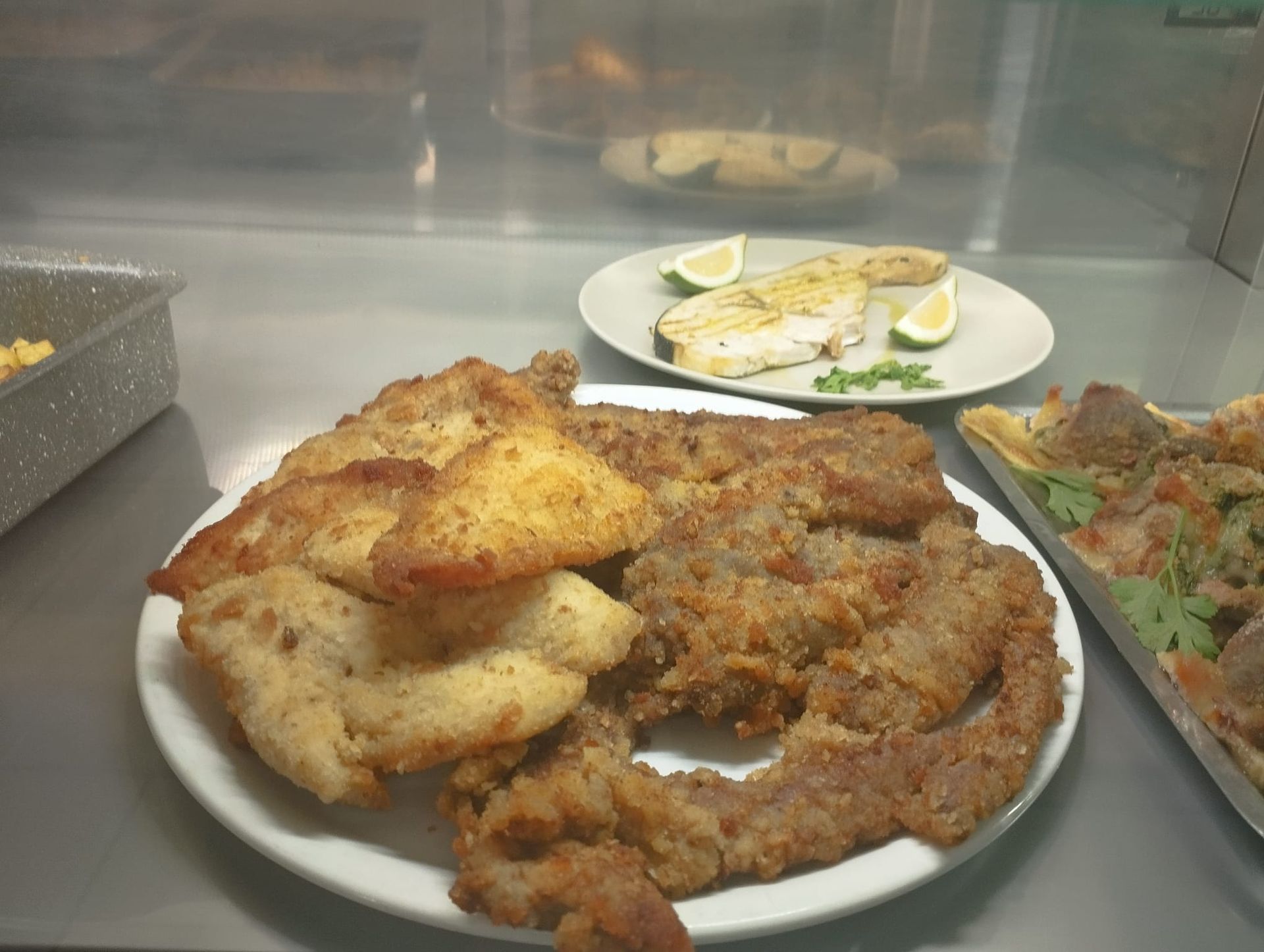 Piatti di cibo fritto su un bancone, tra cui cotolette impanate, pesce fritto e un vassoio di contorni preparati.