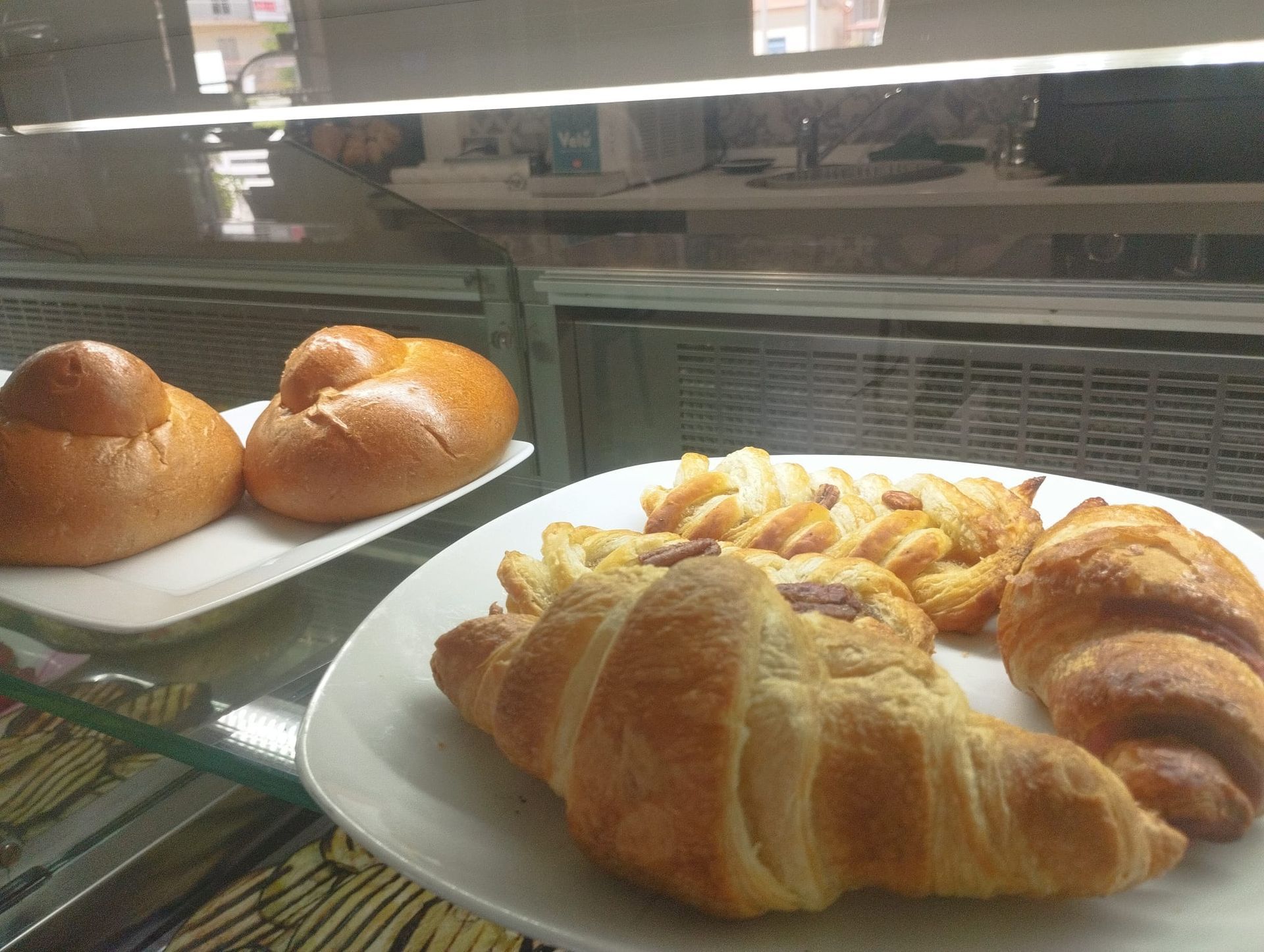 Primo piano dell'esposizione di un panificio: croissant e brioche su piatti bianchi all'interno di una teca di vetro.