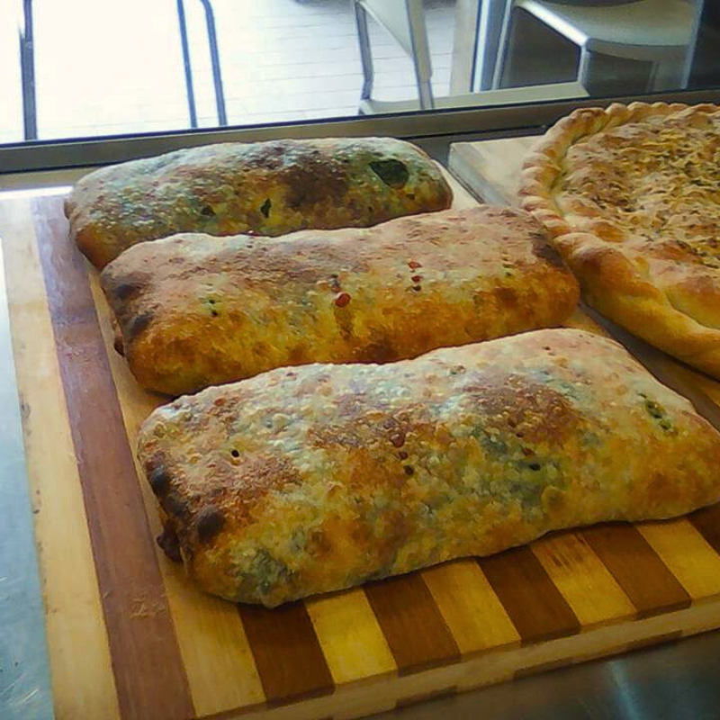 Tre pasticcini rettangolari, dorati e cotti al forno, probabilmente ripieni di verdure, sono adagiati su un tagliere di legno a strisce.