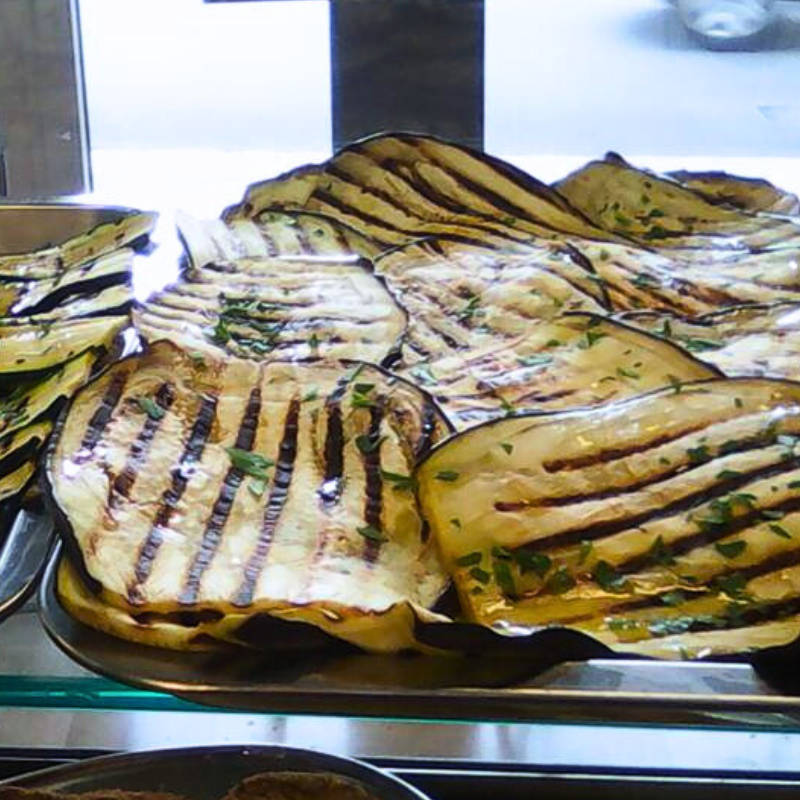 Fette di melanzane grigliate su una teglia di metallo, con i segni della griglia ben visibili e una spolverata di prezzemolo.