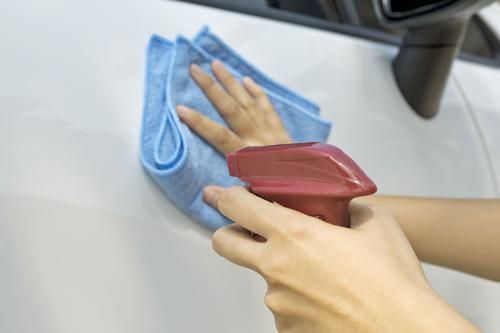 A person is cleaning a car with a towel and spray bottle.