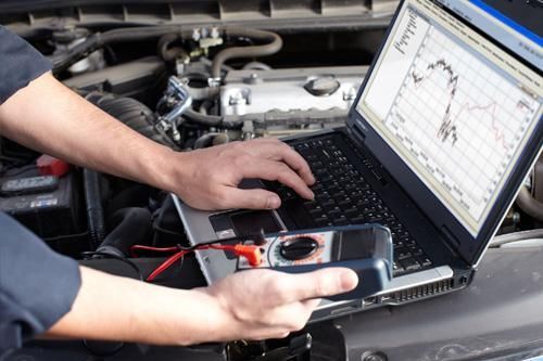 A man is using a laptop computer under the hood of a car.