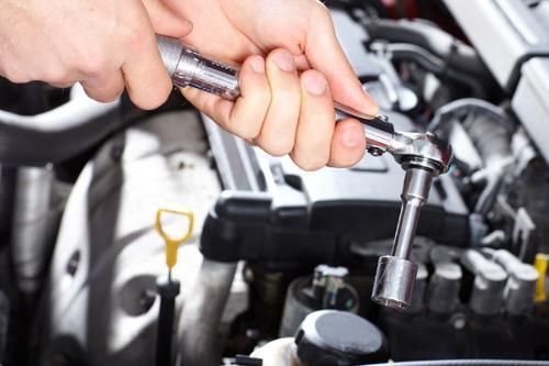 A person is working on a car engine with a wrench.