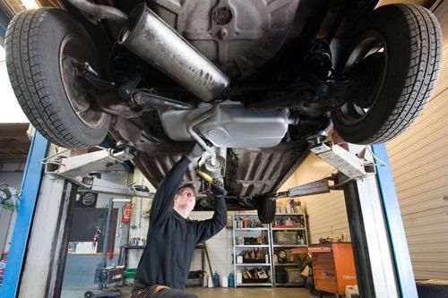 A man is working under a car on a lift in a garage.