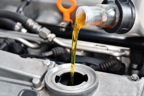 A close up of a person pouring oil into a car engine.