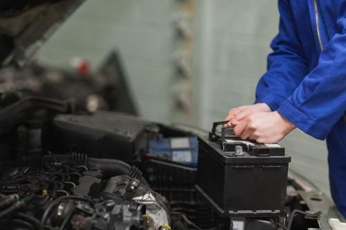 A mechanic is working on a car battery in a garage.