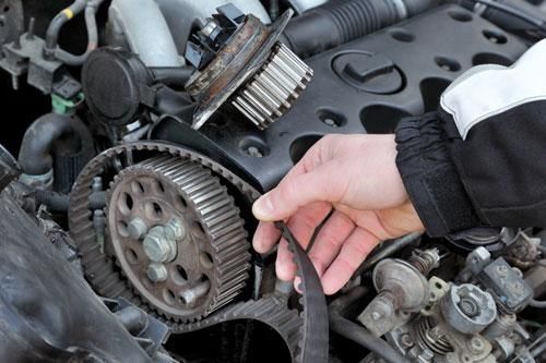 A person is cleaning a belt on a car engine with a brush.