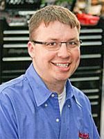 A man wearing glasses and a blue shirt is smiling for the camera.