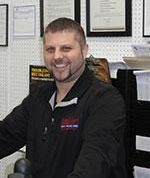 A man is smiling while sitting at a desk in an office.