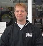 A man in a black jacket is standing in front of a window.