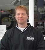 A man in a black jacket is standing in front of a window.