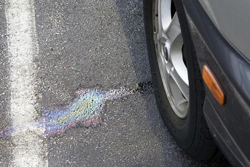 A car is parked in a parking lot with a rainbow of oil on the ground.