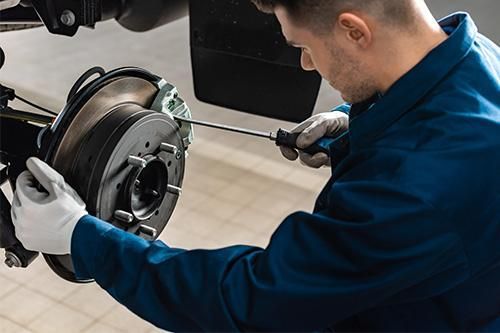 A man is fixing a brake on a truck with a screwdriver.