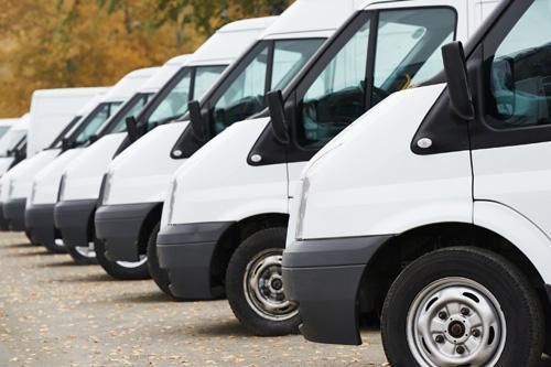 A row of white vans parked next to each other in a parking lot.