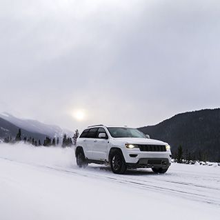 A white jeep is driving through the snow on a snowy road.