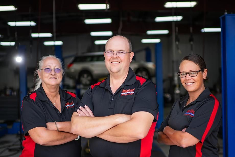 Three people are posing for a picture in a garage with their arms crossed.