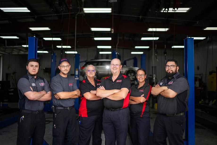 A group of mechanics are posing for a picture in a garage.