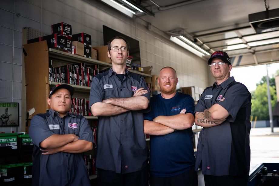 A group of men are standing in a garage with their arms crossed.