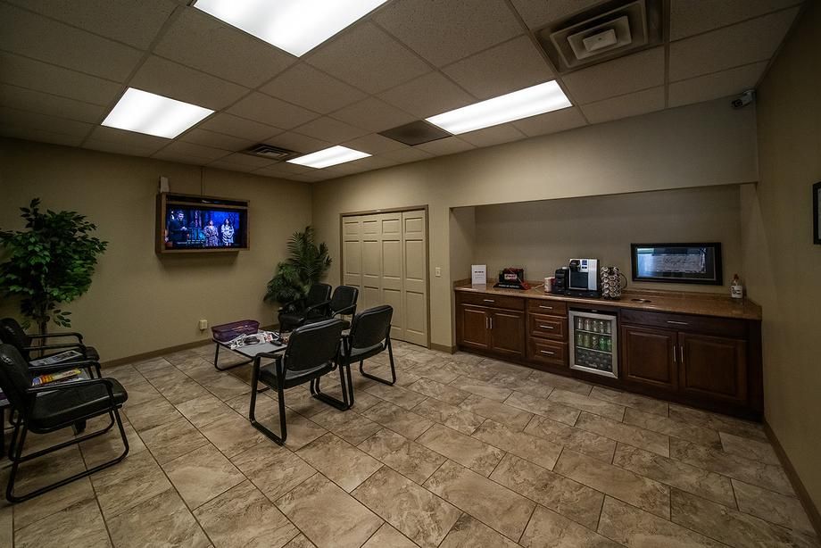 A waiting room with chairs , a television and a refrigerator.