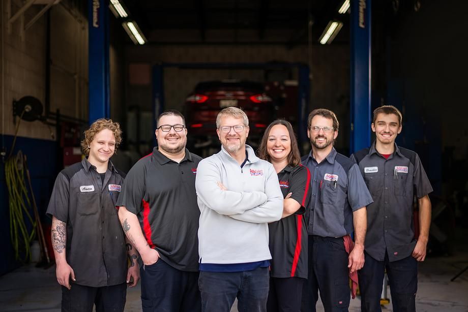 A group of mechanics are posing for a picture in a garage.