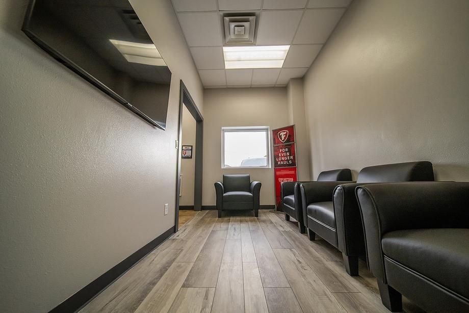 A waiting room with chairs , a flat screen tv and a vending machine.