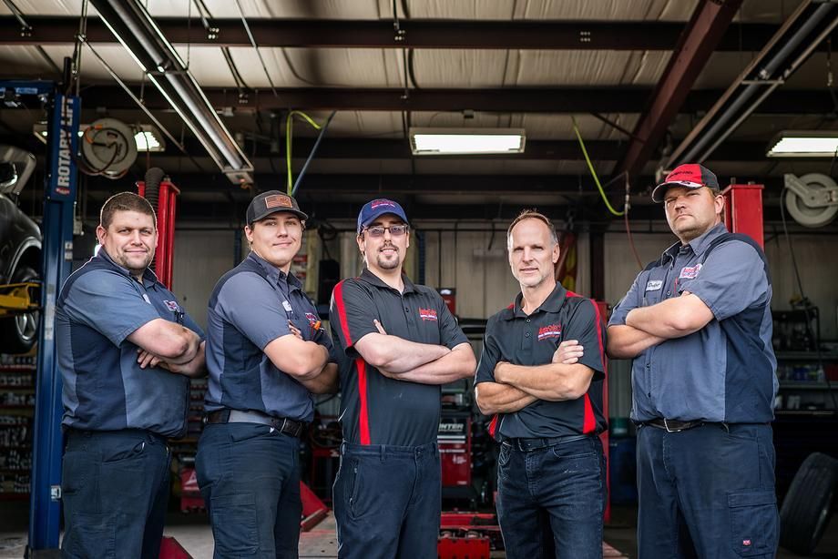 A group of mechanics are posing for a picture in a garage.