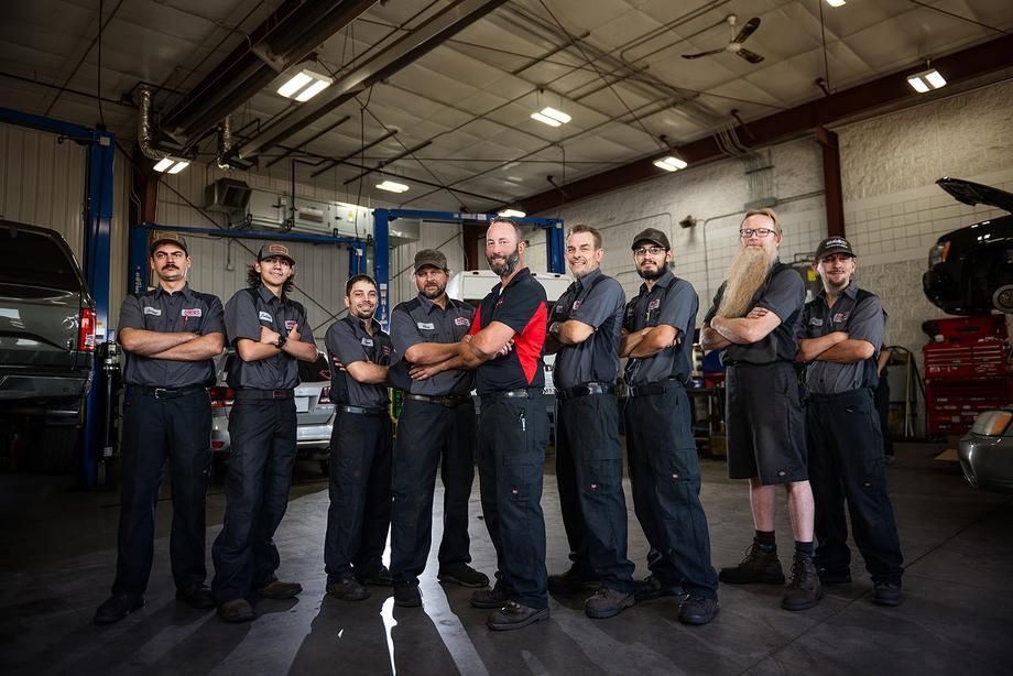 A group of mechanics are posing for a picture in a garage.