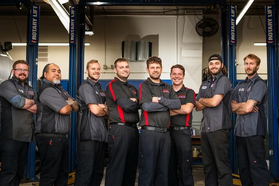 A group of mechanics are posing for a picture in a garage.