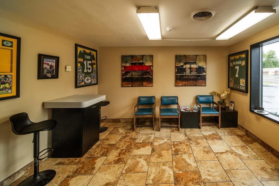 A waiting room with a table , chairs , and paintings on the wall.