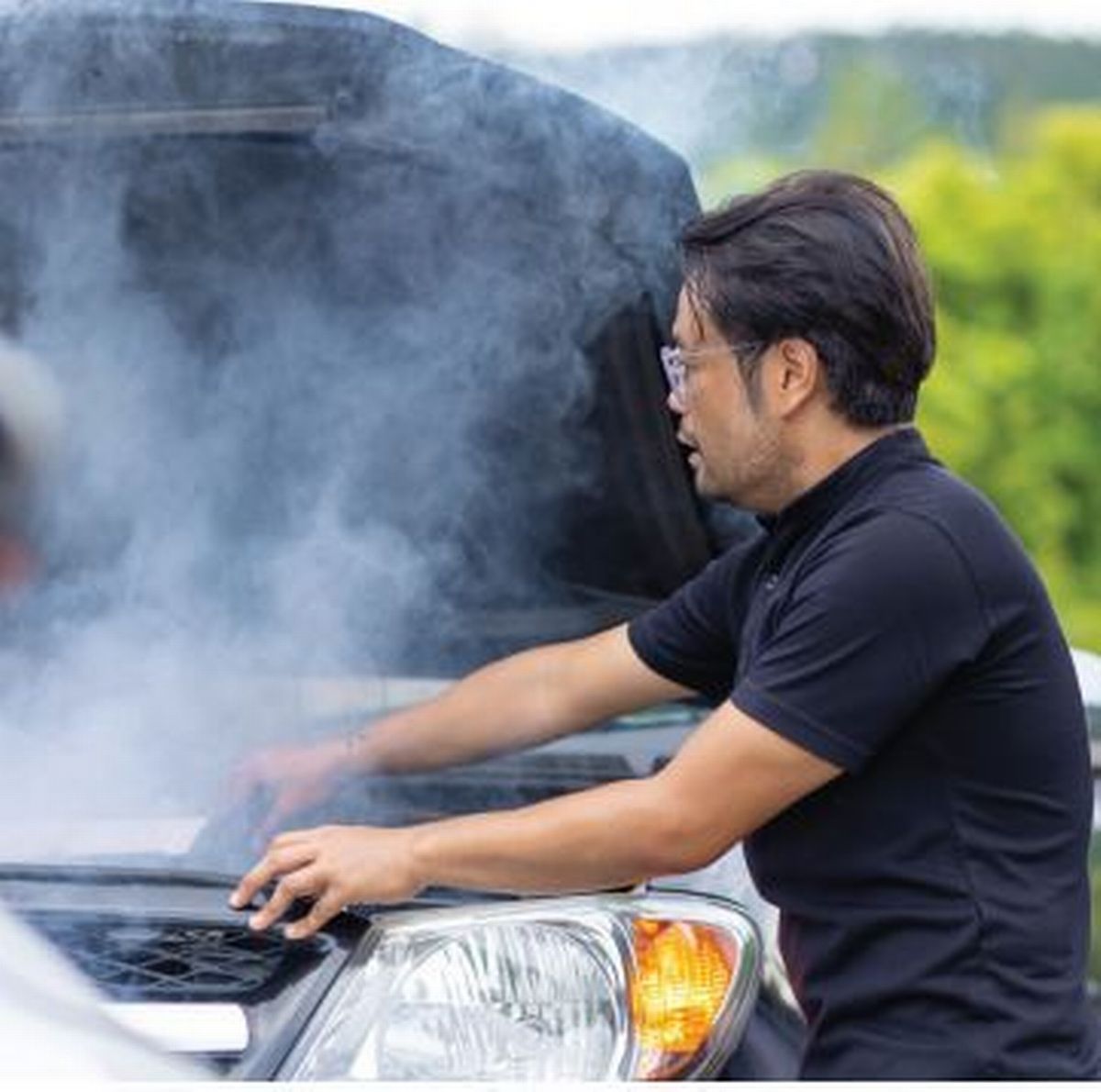 A man is looking under the hood of a car with smoke coming out of it.