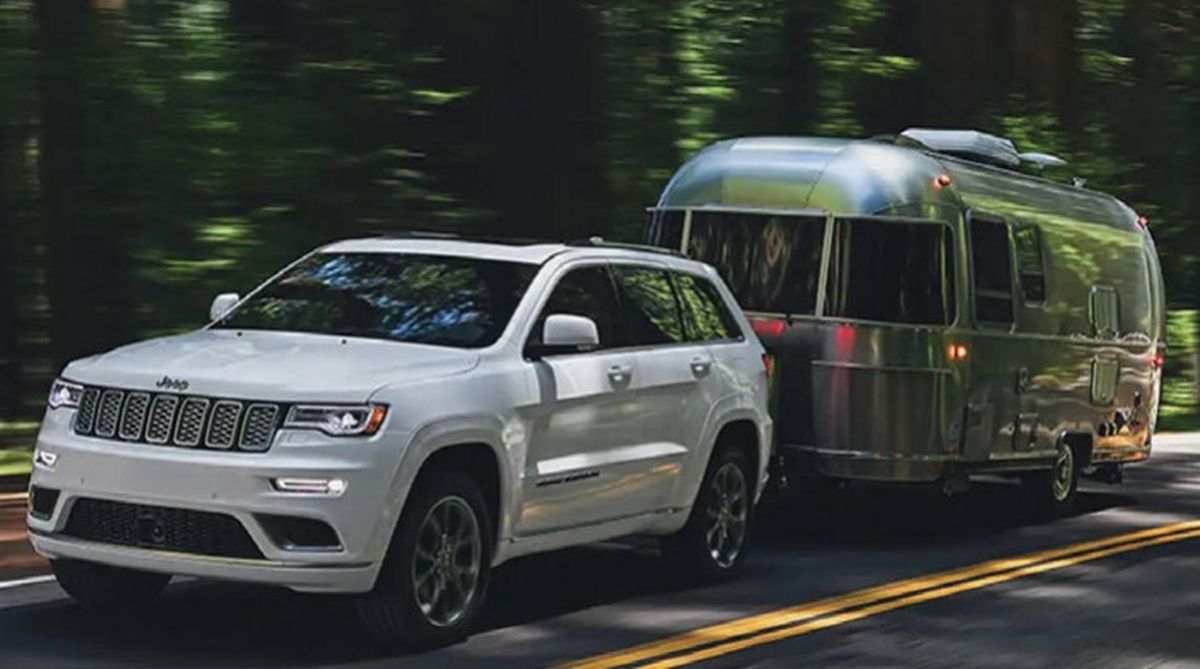 A white jeep is towing a trailer down a road.