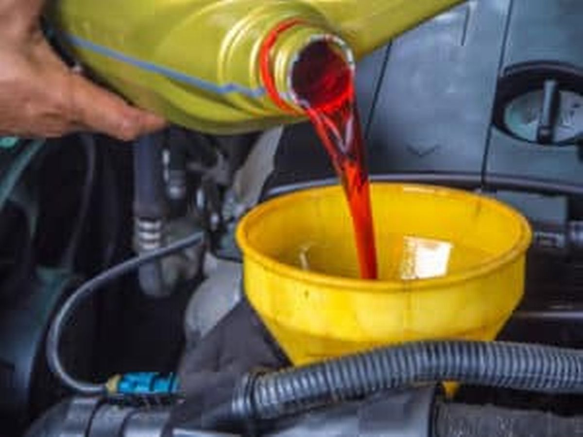 A person is pouring oil into a yellow funnel in a car.