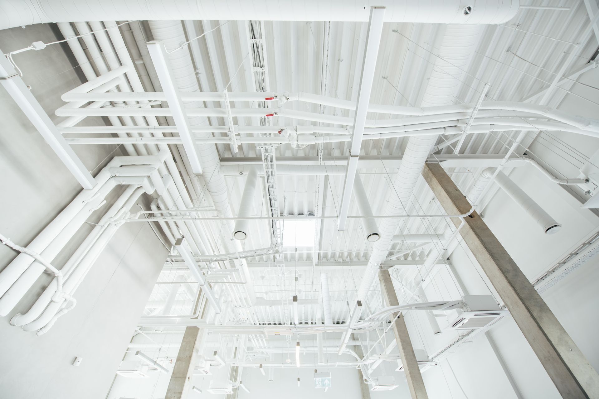 Looking up at the ceiling of a building with pipes and wires.